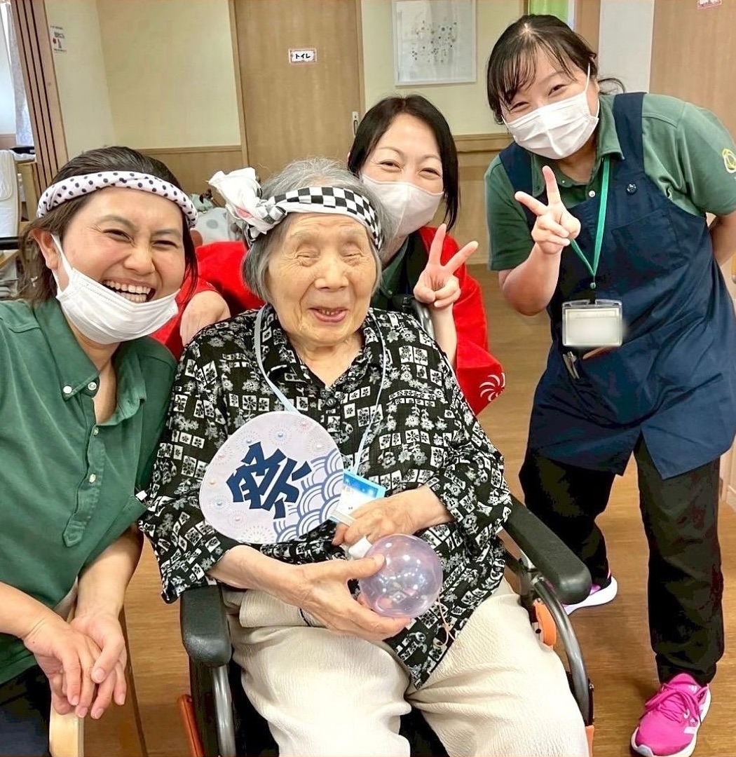 夏祭りの行事ではっぴを着たスタッフと利用者が笑顔で写る様子