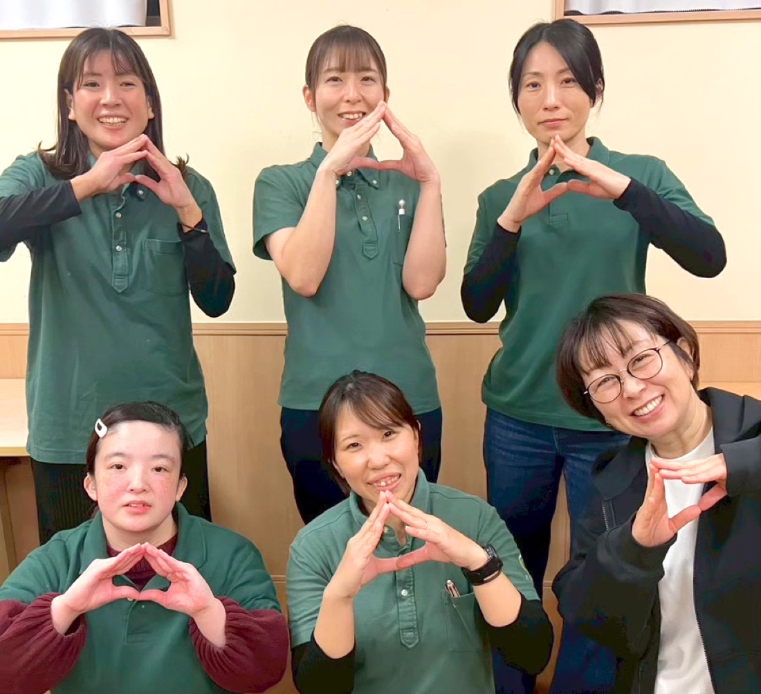 「おむすび」のポーズで笑顔を見せるスタッフたち